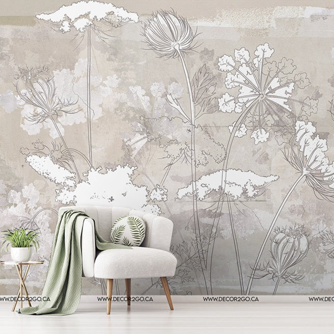 A living room wall covered with a Decor2Go Wallpaper Mural featuring delicate line drawings of various flowers. In front, a modern white armchair with green pillows and a small table with a plant.