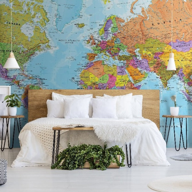 A cozy bedroom decorated with Decor2Go Wallpaper Mural's Bright World Map Wallpaper Mural, featuring a bed with white linens, side tables, lamps, and a variety of potted plants and framed art.