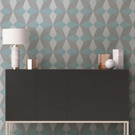 A modern dark grey sideboard against a Aqua Cerium Concrete Geometric Wallpaper (56 SqFt) by York Wallcoverings, decorated with a white lamp and minimalist accessories.
