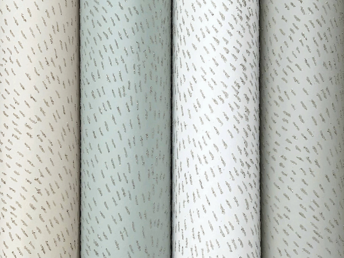 Four vertical rolls of York Wallcoverings' Dew Drop Grey Wallpaper (60 SqFt) in muted beige, green, and white shades, each featuring subtle diagonal silver dash patterns across the non-woven surface.