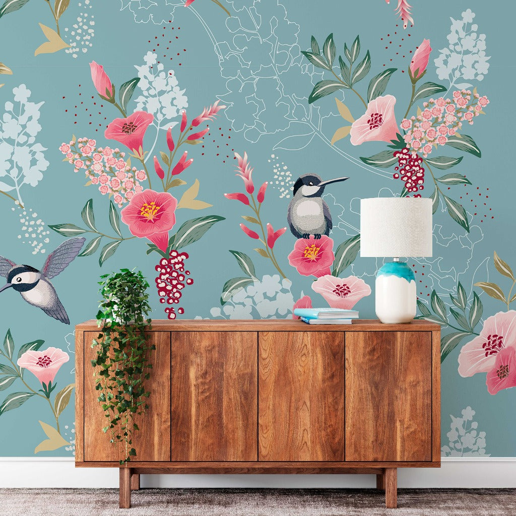 A stylish room with a Decor2Go Wallpaper Mural in shades of blue, pink, and green. A wooden cabinet with a lamp, books, and plants decorates the space.