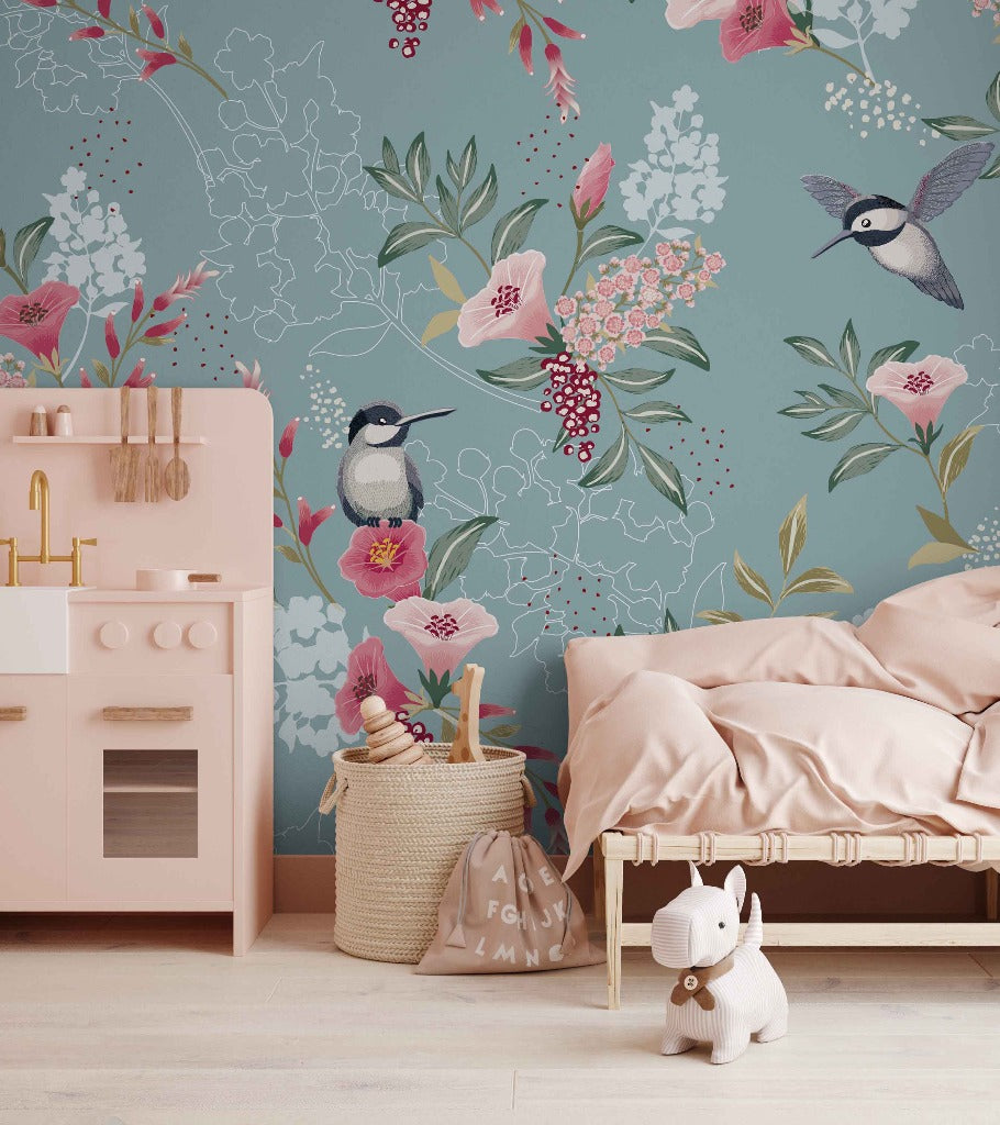 A cozy children's room with a pastel pink bed and a wooden play kitchen. The walls are adorned with a Decor2Go Wallpaper Mural in shades of blue and pink featuring hummingbirds and florals.