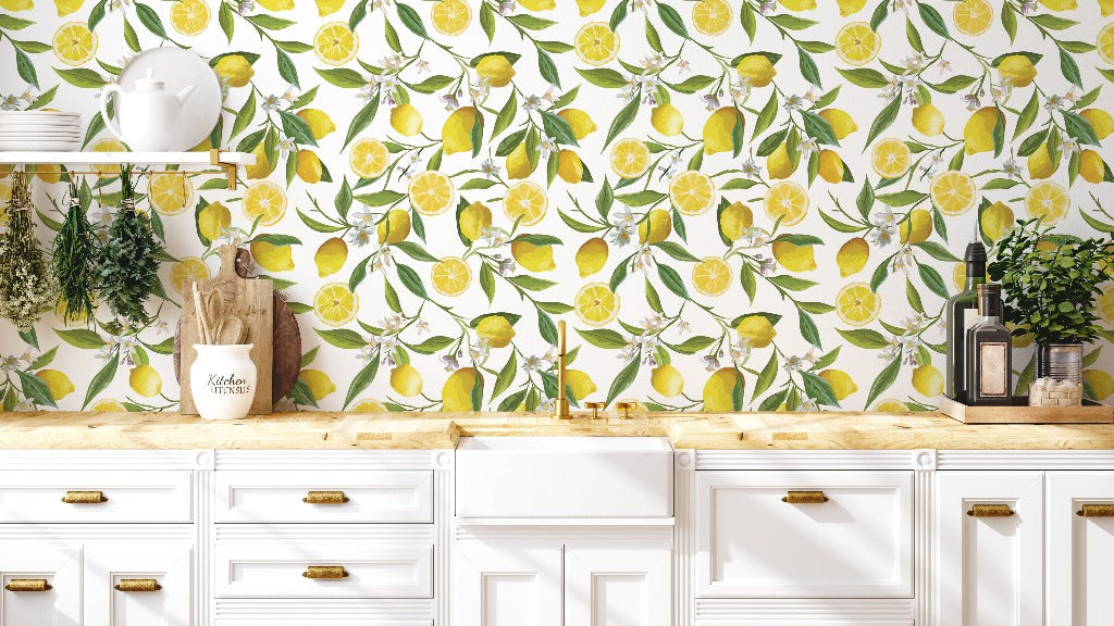 A bright and airy kitchen features a cheerful yellow Decor2Go Wallpaper Mural with an If Life Gives You Lemons Wallpaper Mural. White cabinets with brass handles are topped with a wooden countertop. The counter has a cutting board, jars, and fresh herbs hanging on a shelf. The decor captures an optimistic and lively feel.