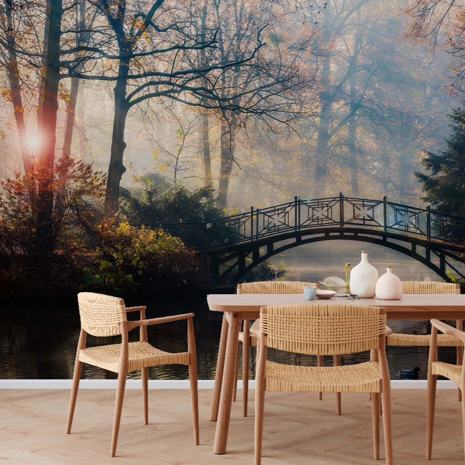 Outdoor dining setup with a wooden table and chairs overlooking a serene pond with a Romantic Bridge Wallpaper Mural from Decor2Go Wallpaper Mural, surrounded by autumn trees bathed in soft, magical sunlight.