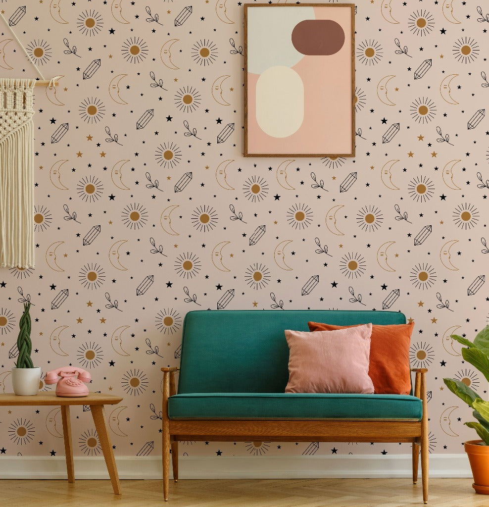 A cozy living room with a teal sofa adorned with pink and orange cushions. The wall behind showcases a whimsical Decor2Go Wallpaper Mural Sun and Moon Wallpaper Mural, complete with stars and comet patterns. A framed abstract art piece and a small wooden table complete the celestial design theme.