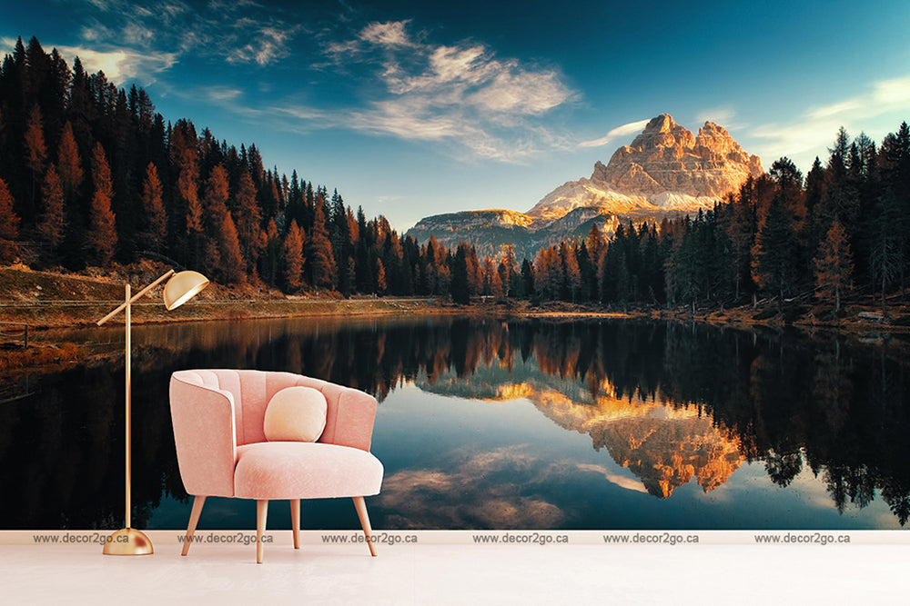 A pink armchair next to a lamp, situated outdoors by a Decor2Go Wallpaper Mural, reflecting mountains and trees under a clear sky at sunset.