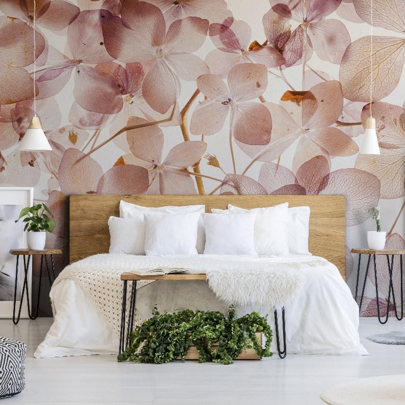 A cozy bedroom featuring a wooden bed with white bedding, flanked by plants and eclectic decor, against a feminine Decor2Go Wallpaper Mural wall. Shelves with books and decor items enhance the inviting ambiance.