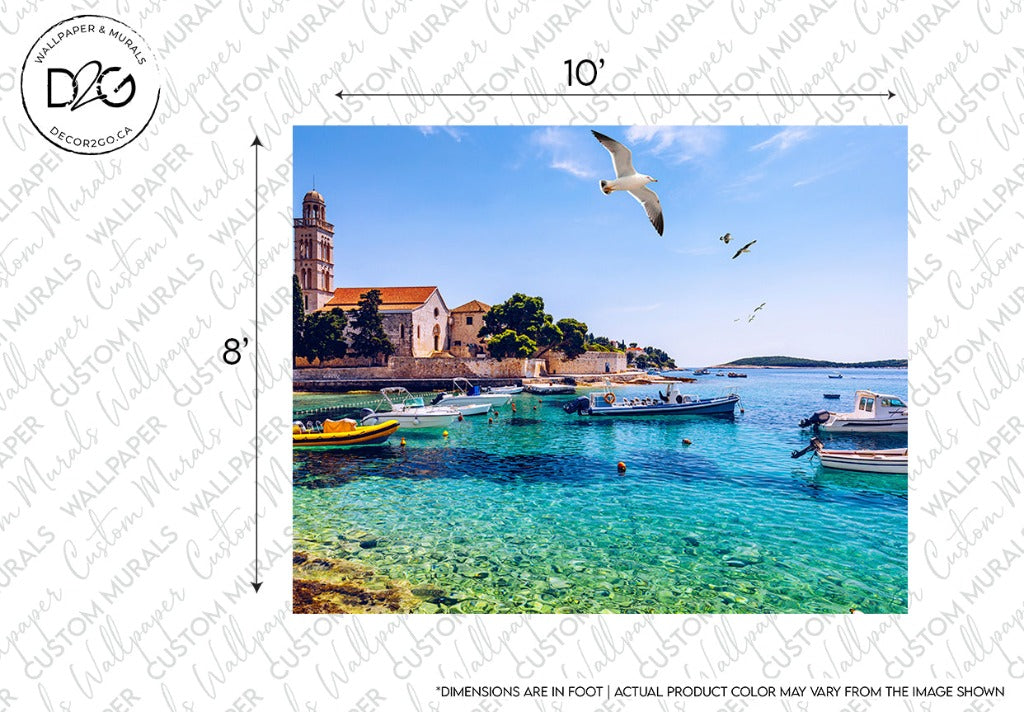 A serene coastal scene features clear turquoise waters and moored boats. A stone church and lush greenery rest upon the shore, while seagulls fly overhead under a bright blue sky. The Riviera Wallpaper Mural by Decor2Go Wallpaper Mural captures a peaceful Mediterranean setting with custom sizing available for your space.