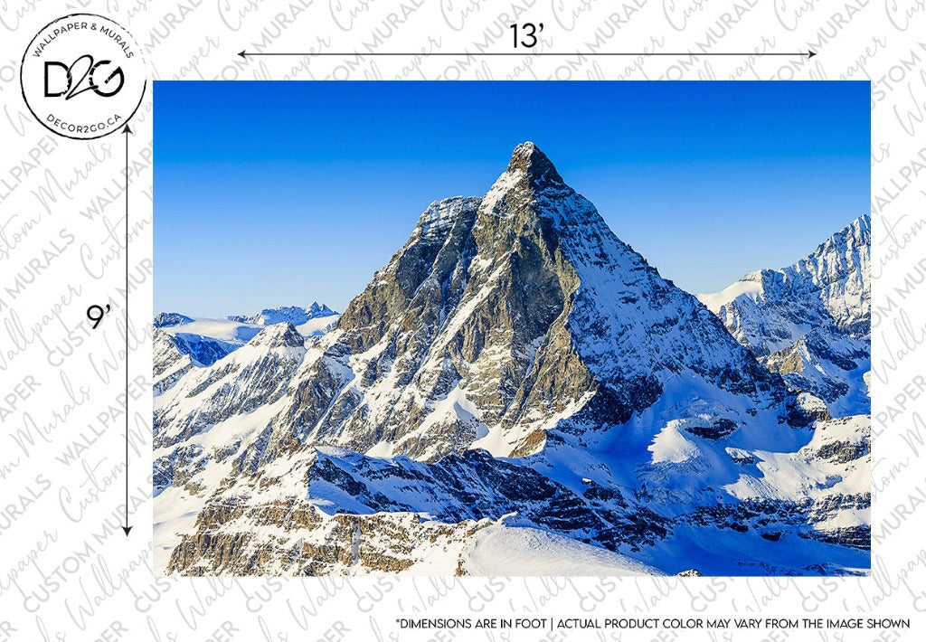 A majestic, snow-covered Matterhorn mountain range under a clear blue sky, with sunlight illuminating its rugged surface. The lower slopes show scattered shadows and varying textures of snow and rock. This scene is captured perfectly in the Decor2Go Wallpaper Mural.