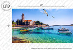 A picturesque coastal scene featuring a small church with a tower, lush greenery, and several boats floating on clear turquoise water. A seagull flies in the blue sky above. This Decor2Go Wallpaper Mural: Riviera Wallpaper Mural captures the charm and serenity of coastal life. Dimensions are labeled as 16' by 9'.