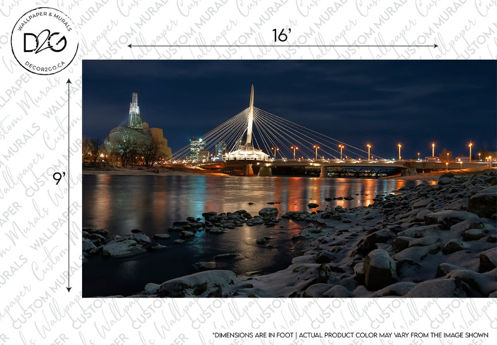 A serene night landscape of a cityscape with a distinctive cable-stayed bridge lit up, reflecting on a river's surface, with ice-covered rocks along the shoreline in the foreground featuring the Decor2Go Wallpaper Mural "Winnipeg in Blues.
