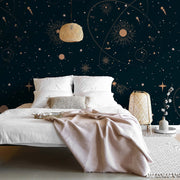 Bedroom - A cozy bedroom with a white bed and beige blanket, against a dark blue Decor2Go Wallpaper Mural featuring planets and constellations. A woven nightstand and lamp complement the scene.
