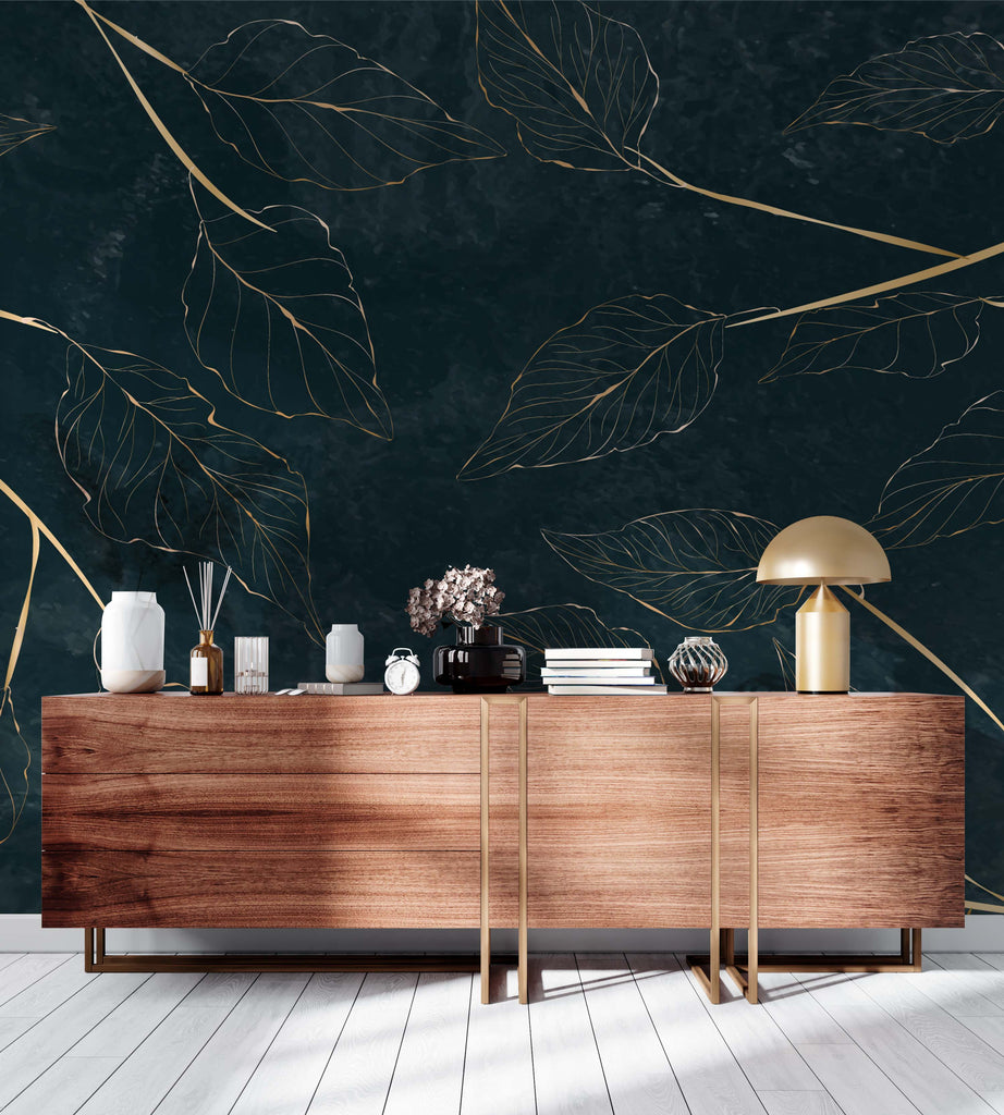 A stylish wooden sideboard against a dark blue wall adorned with Decor2Go Wallpaper Mural featuring gold leaf designs. The sideboard is decorated with vases, books, a clock, and a lamp.