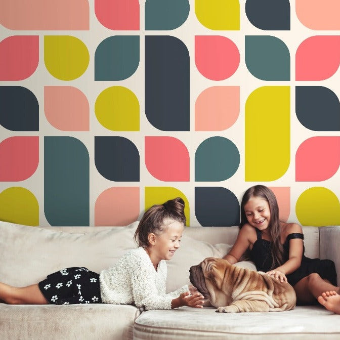 Two girls laughing and playing with a dog on a couch in front of a colorful Decor2Go Wallpaper Mural.