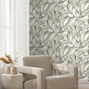 A modern living space features a textured beige armchair, a round side table with a vase of dried flowers, and York Wallcoverings’ Achate Black & Grey Wallpaper (60 SqFt) for a stylish, marbled accent wall.