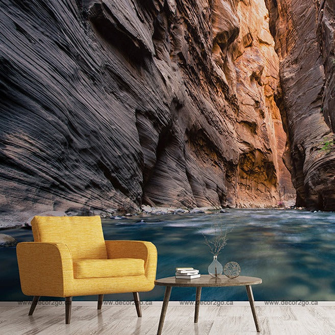A digitally manipulated room with a bright yellow armchair and a small coffee table set against a surreal background of Adventure Canyon Wallpaper Mural, featuring towering rock walls and a serene river by Decor2Go Wallpaper Mural.
