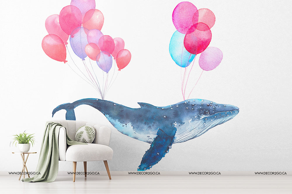 Bedroom - A whimsical mural, perfect for children's bedroom decor, features a large blue whale floating in the air, lifted by multiple colorful balloons in pink and blue shades. The Decor2Go Wallpaper Mural's Air Balloon Whale Wallpaper Mural is displayed in a softly-lit modern room with a white armchair, white cushion, and a side table holding a plant.