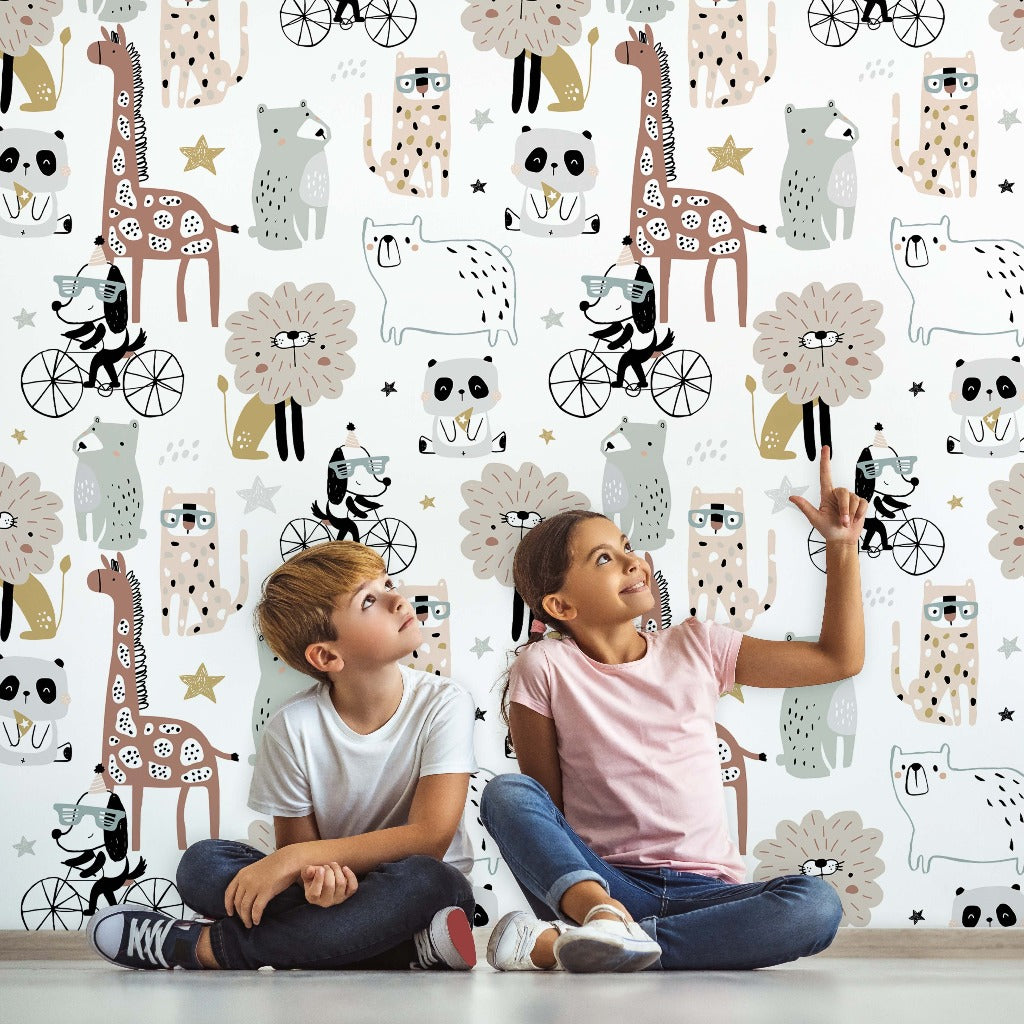 Two children, a boy and a girl, sit on the floor pointing at the Decor2Go Wallpaper Mural featuring playful animals and bicycles in a vibrant color palette. The girl is wearing a pink