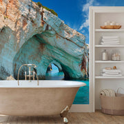 Bathroom - The tranquil bathroom includes a freestanding tub set on wooden floors. The wall is adorned with the Decor2Go Wallpaper Mural's Aquatic Cavern Wallpaper Mural, featuring a breathtaking scene of a coastal rock arch with turquoise waters and sky, seamlessly merging the indoor space with nature. Nearby shelves conveniently store towels and toiletries.