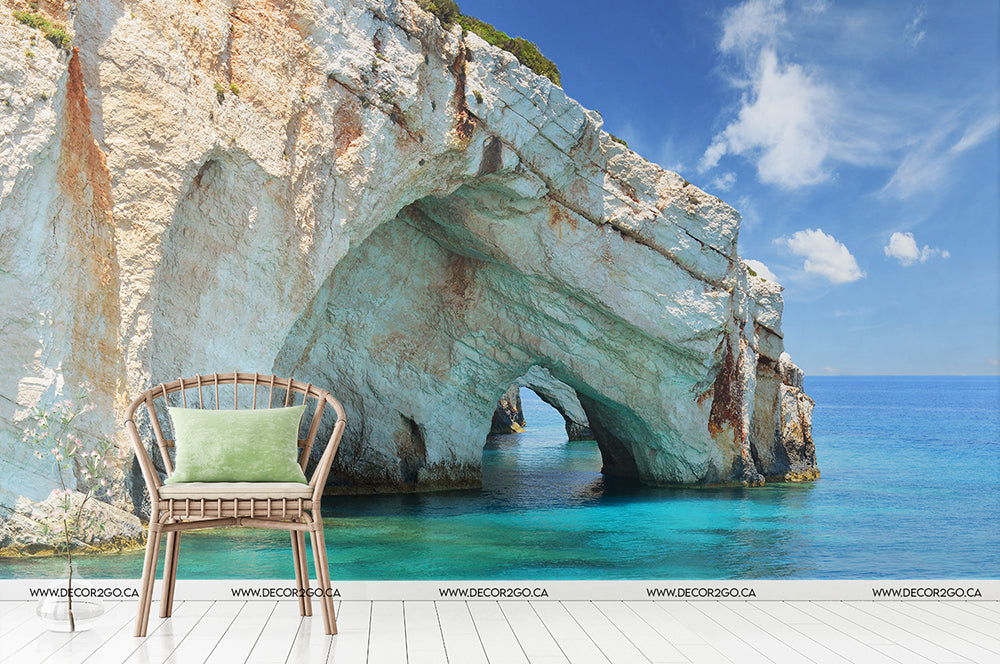 A tranquil scene featuring a green chair on a wooden dock overlooking a bright azure sea framed by a large natural rock arch with Aquatic Cavern Wallpaper Mural from Decor2Go Winnipeg in the background.