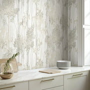 A modern kitchen with light cabinets, gold handles, marble countertop, stacked plates, glass vase with greenery, cutting board, and Aspen Grove Grey Wallpaper (60 SqFt) by York Wallcoverings featuring an abstract neutral forest pattern.