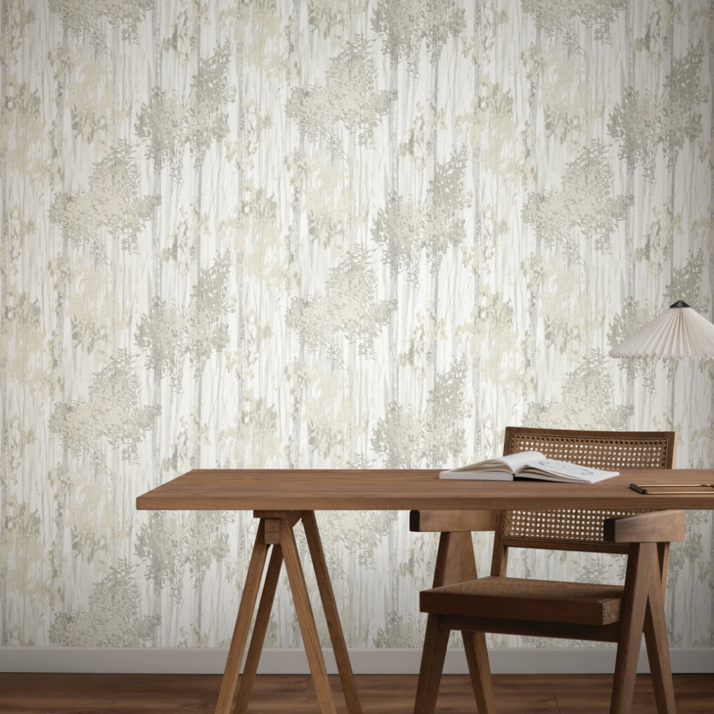 A wooden desk with an open book and a woven chair sits against a wall covered in York Wallcoverings' Aspen Grove Grey Wallpaper (60 SqFt), featuring a subtle abstract pattern. A modern table lamp with a pleated shade is on the right side of the desk.