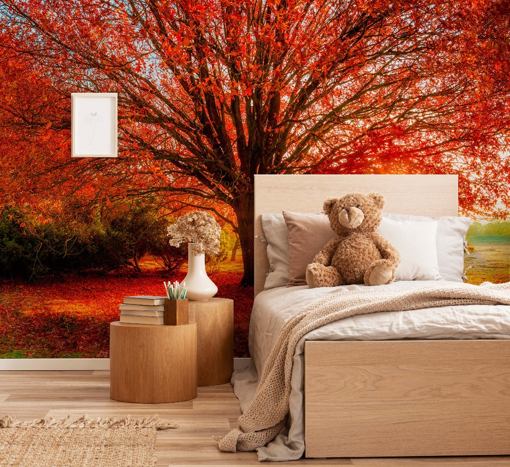 A cozy bedroom with a large bed and a teddy bear on it. The room opens to a vibrant autumn landscape with red and orange foliage, enhancing the room's warm, inviting atmosphere with an Autumn Colours Wallpaper Mural from Decor2Go Wallpaper Mural.