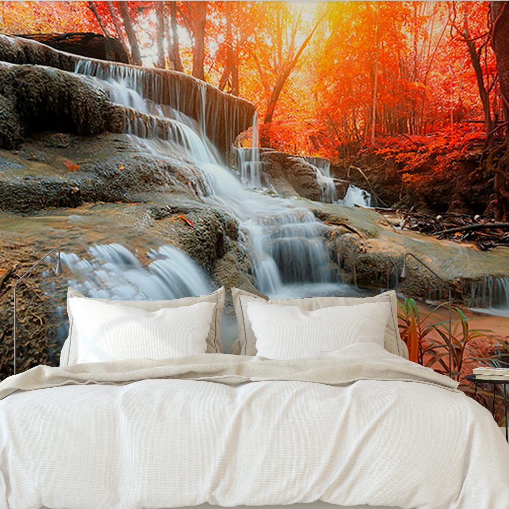 A surreal scene displaying a large, plush white bed positioned in front of a vibrant autumn forest and Autumn Waterfall Wallpaper Mural from Decor2Go Wallpaper Mural, creating a blend of indoor comfort with an outdoor natural landscape.