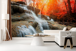 A stylish living room with a Decor2Go Wallpaper Mural of an Autumn Waterfall in a vibrant autumn forest, featuring a white sofa, a round coffee table, and a modern floor lamp.