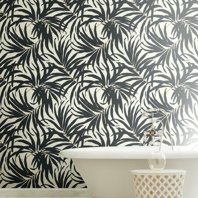 A bathroom adorned with the York Wallcoverings' Black Bali Leaves Wallpaper (60 SqFt) in black and white highlights contemporary design. A sleek, white bathtub with a silver faucet is placed in front, accompanied by a woven basket on the floor to create a serene, nature-inspired atmosphere.