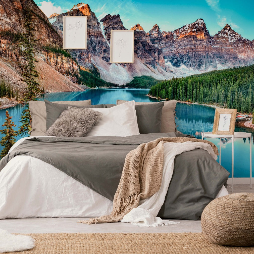 A serene bedroom setup with a comfortable bed draped in white and gray bedding, a cozy blanket, and overlooking a stunning Decor2Go Wallpaper Mural of a lakeside mountain view.