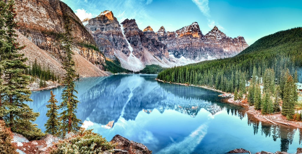 Panoramic view of Moraine Lake in Banff National Park, Canada, featuring mirror-like reflections of snowy mountains and pine trees on serene blue water, perfect for a Decor2Go Wallpaper Mural feature wall that showcases the Banff Panorama Wallpaper Mural.