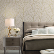 Bedroom - A with a tufted headboard and beige bedding is enhanced by metallic accents. Beside the bed is a nightstand with a lamp, books, and flowers. The room features York Wallcoverings' Beige & Gold Trees Silhouette Wallpaper, adding a subtle tree branch pattern