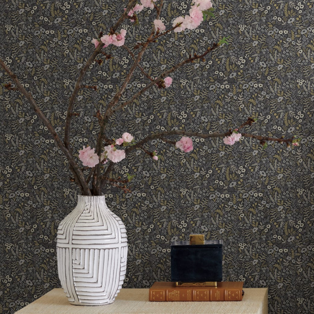 A white vase with geometric patterns holds blooming pink cherry branches on a beige surface, next to two stacked books and a small black box, set against York Wallcoverings Black/Beige Tapestry Wallpaper for an elegant touch.