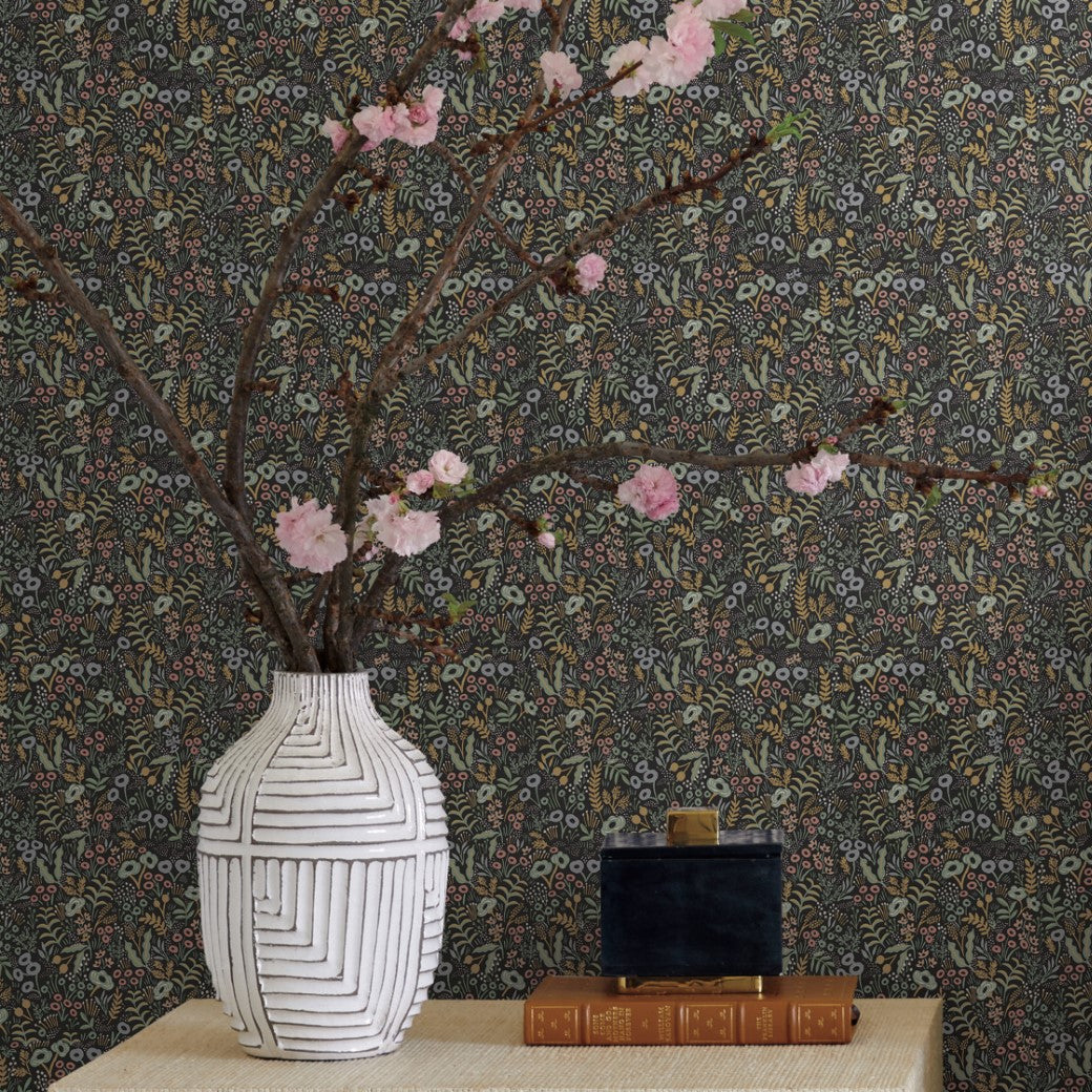 A white vase with geometric patterns holds pink blossoms beside stacked books and a small black container, set against Black Tapestry Wallpaper (60 SqFt) by York Wallcoverings.
