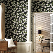 A room features York Wallcoverings Black/White Hydrangea Wallpaper (60 SqFt), white wainscoting, a column, and a wicker bench. Through French doors, a study with geometric wallpaper, desk, lamp, and floral arrangement is visible.
