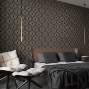 Bedroom - A modern features York Wallcoverings' Black & Gold Harlowe Wallpaper with geometric design, a large bed with dark pillows, gray blanket, two cushioned chairs in the foreground, and a vertical pendant light from the Modern Metals Collection adding a contemporary touch