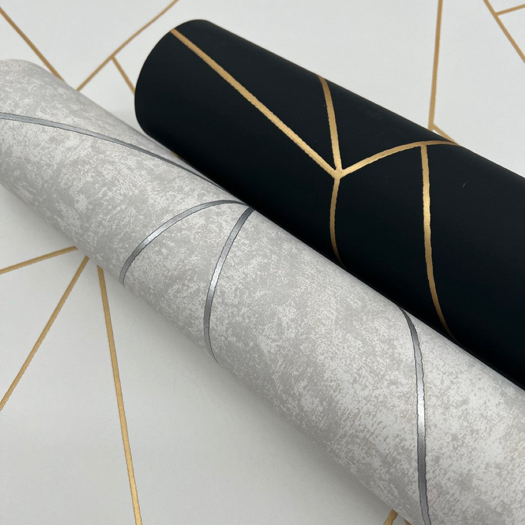 Displayed are two rolls of York Wallcoverings' Nazca Wallpaper. One roll is Black & Gold with metallic gold geometric lines, while the other is textured light gray with a silver geometric design, all set against a similar gold pattern backdrop.