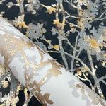 A close-up of York Wallcoverings' Black & Multi Shimmering Foliage Wallpaper (57 SqFt) reveals a sophisticated floral pattern in metallic gold and gray against a dark backdrop, featuring intricate flowers and branches.