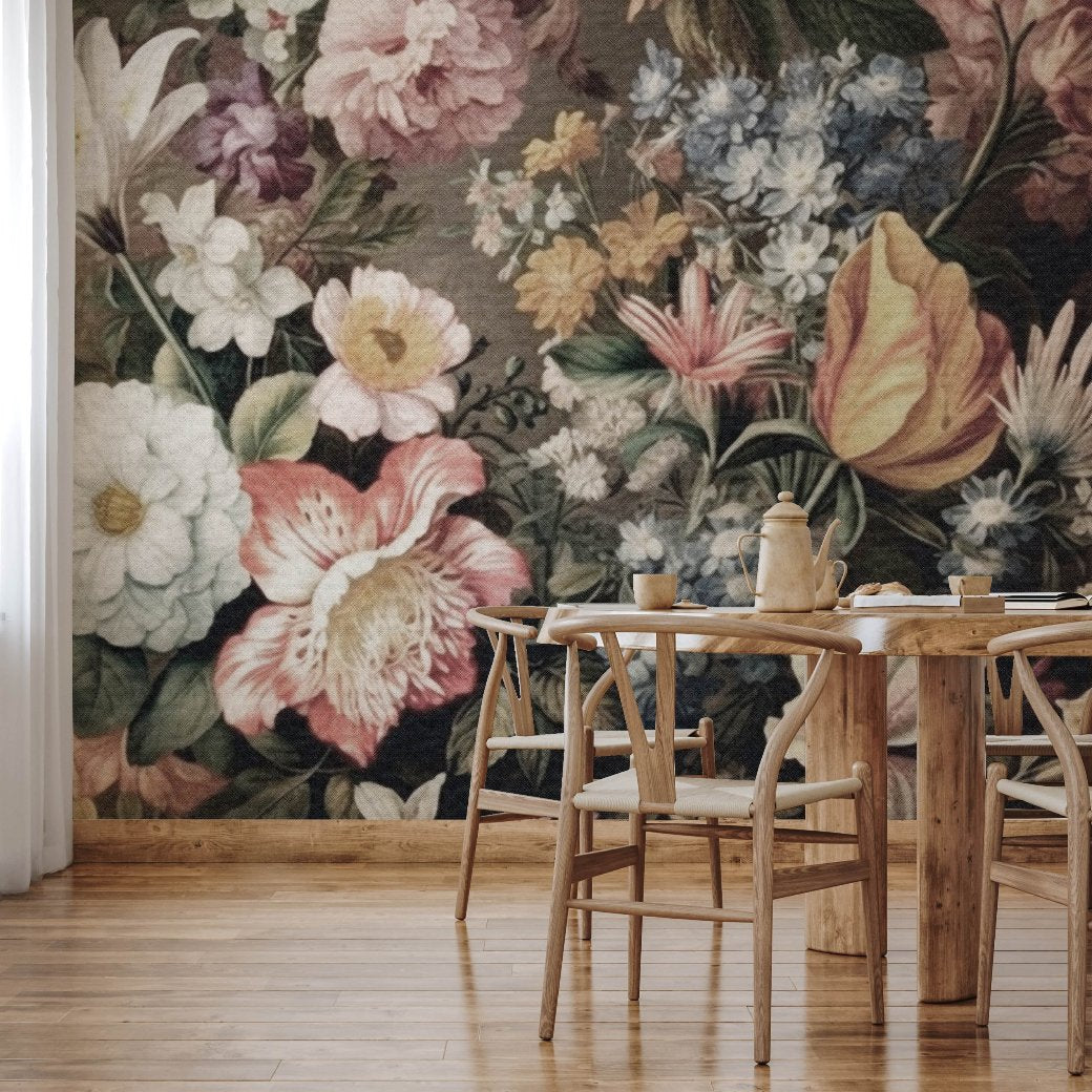 A wooden dining table with matching chairs sits in a room adorned by the large, colorful Blooming Meadow Wallpaper Mural by Decor2Go. This mural features various flowers in pink, yellow, and blue hues. The room is completed with wooden flooring and white curtains.