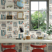 Home Office - A bright with two red chairs, a white desk, a black lamp, and York Wallcoverings’ Blue/Red City Maps Wallpaper (60 SqFt), showcasing maps of cities like Paris and New York. A large window frames lush greenery; shelves hold books and decor