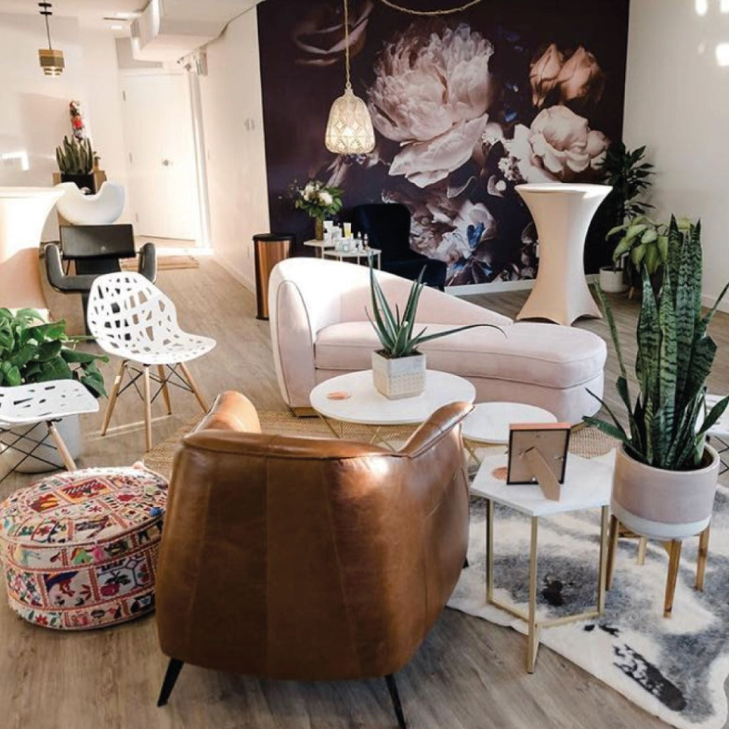 A stylish lounge area with pastel-colored sofas, a large floral wall mural featuring the Decor2Go Wallpaper Mural of white peonies, eclectic chairs, and functional decor like green potted plants, all under soft, warm lighting.