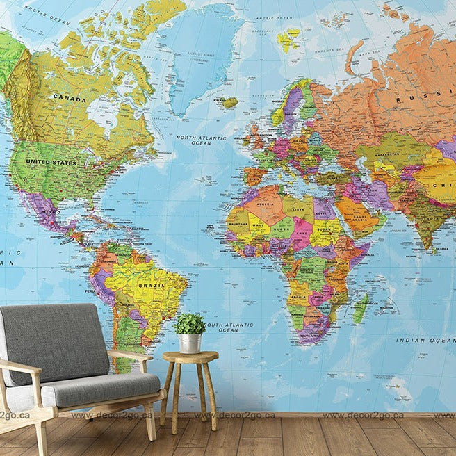A Decor2Go Wallpaper Mural, brightly colored Bright World Map Wallpaper Mural, covers an entire wall, with a gray armchair and a small wooden side table next to it, in a room with light wooden floors.