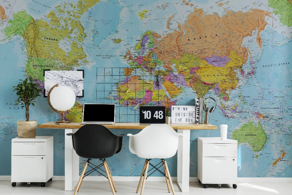 A modern office space with a large Decor2Go Wallpaper Mural of Bright World Map on the wall, featuring a wooden desk with a computer, two black chairs, and a small potted plant.