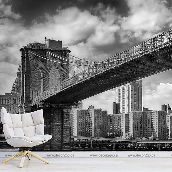Black and white image blending a room setting with an urban backdrop, featuring a stylish chair and lamp in a living space superimposed on a Decor2Go Wallpaper Mural and Manhattan skyline.