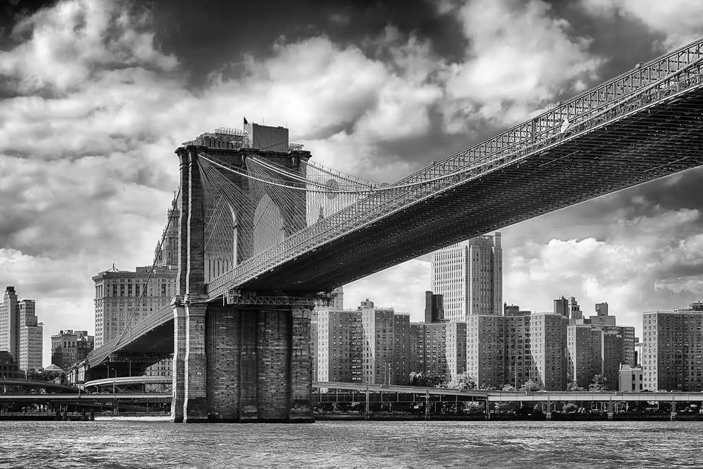 Black-and-white Decor2Go Wallpaper Mural of the Brooklyn Bridge spanning over the East River with the Manhattan skyline in the background, under a cloudy sky.