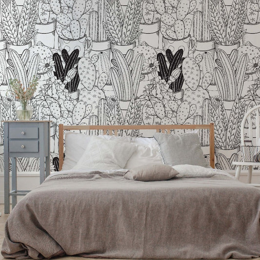 A cozy bedroom featuring a wooden bed with grey bedding, a white chair, a grey nightstand, and walls covered in Decor2Go Wallpaper Mural's Cactus Clan Wallpaper Mural.