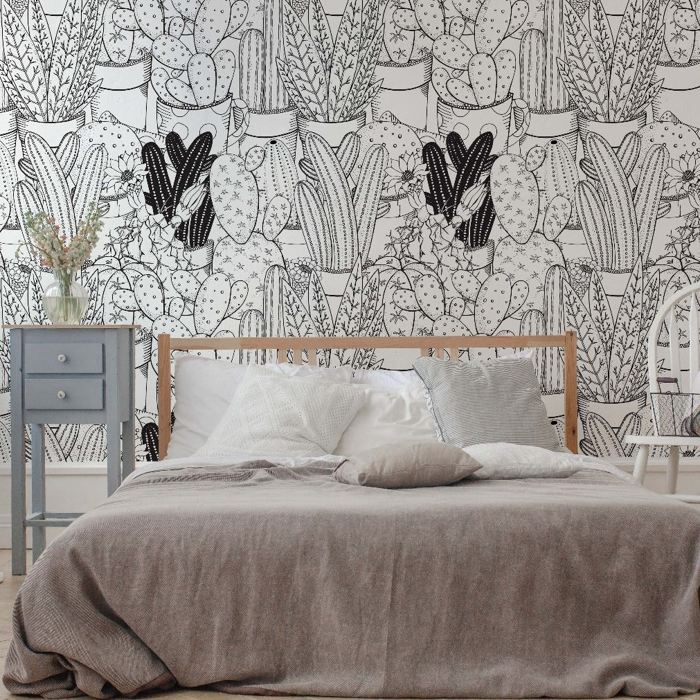 A cozy bedroom featuring a wooden bed with grey bedding, a white chair, a grey nightstand, and walls covered in Decor2Go Wallpaper Mural's Cactus Clan Wallpaper Mural.