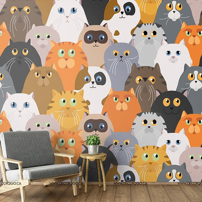 A colorful room with a wall decorated in a pattern of Decor2Go Wallpaper Mural Cat Party Wallpaper Mural in various hues and expressions. A modern gray armchair and a small wooden side table are placed against the wall.