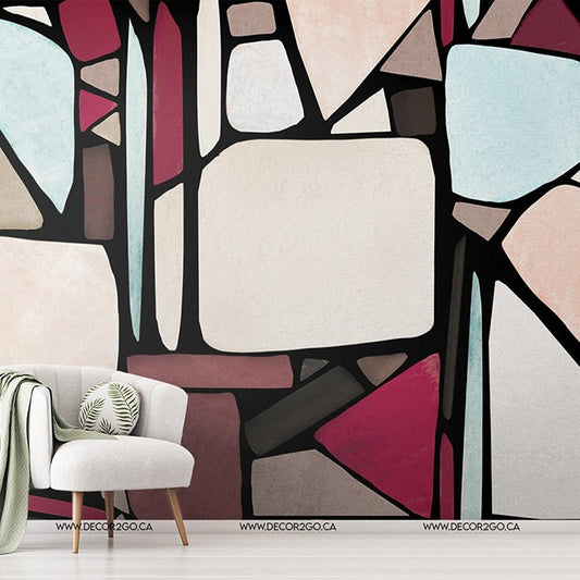 An artistic room with a modern Chic Mosaic Wallpaper Mural from Decor2Go featuring geometric shapes in soft colors. A white chair, green throw blanket, and a side table with plants complete the chic aesthetic interior.